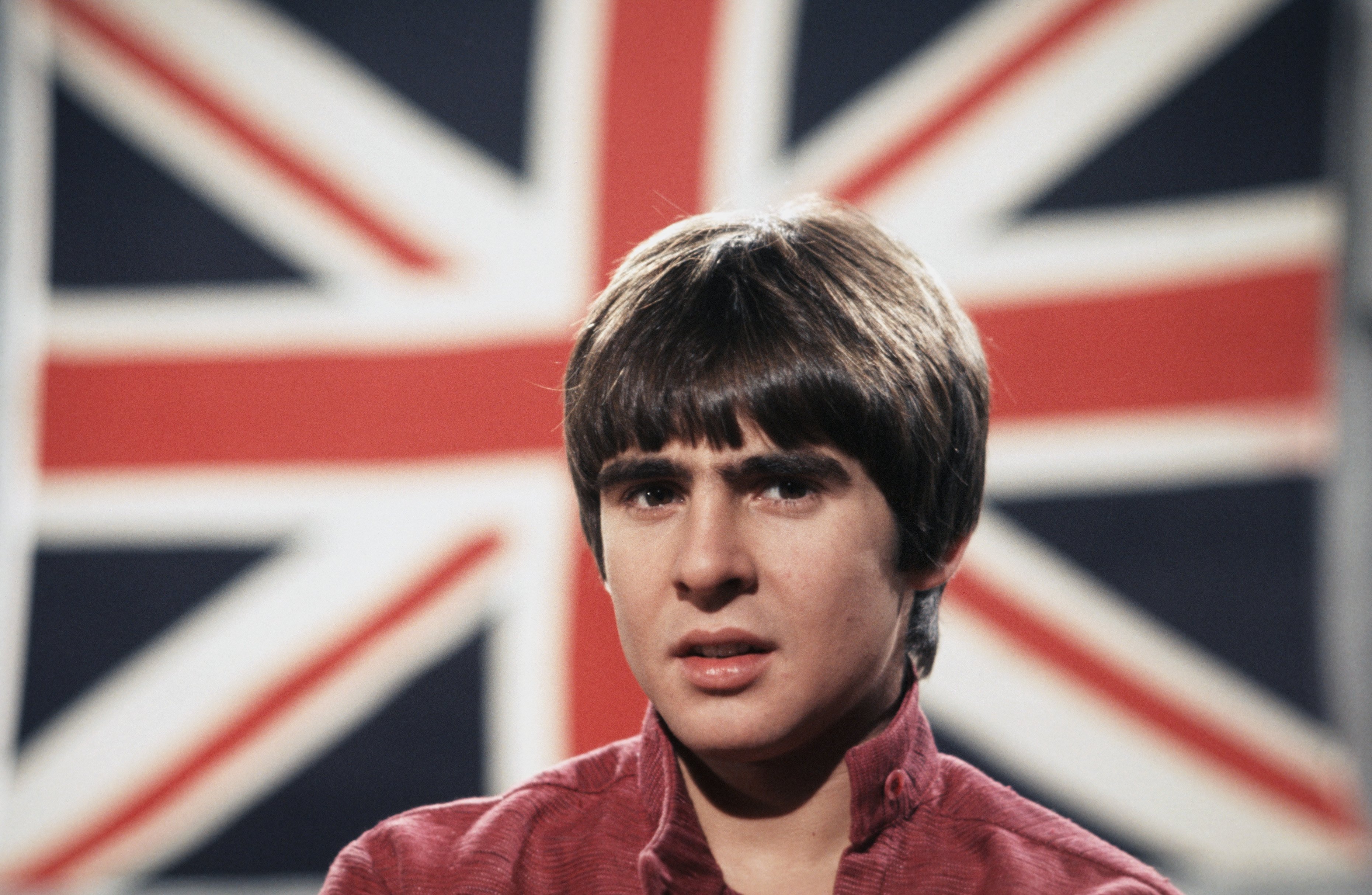 Davy Jones, vocalist of The Monkees' "I Wanna Be Free," in front of a flag