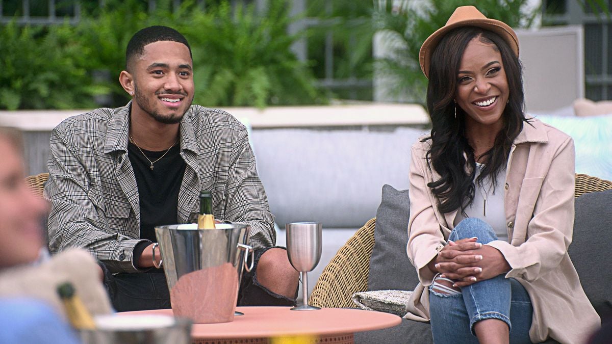 Randall and Shanique of The Ultimatum cast sit on chairs near a bottle of champagne and a metal wine glass.