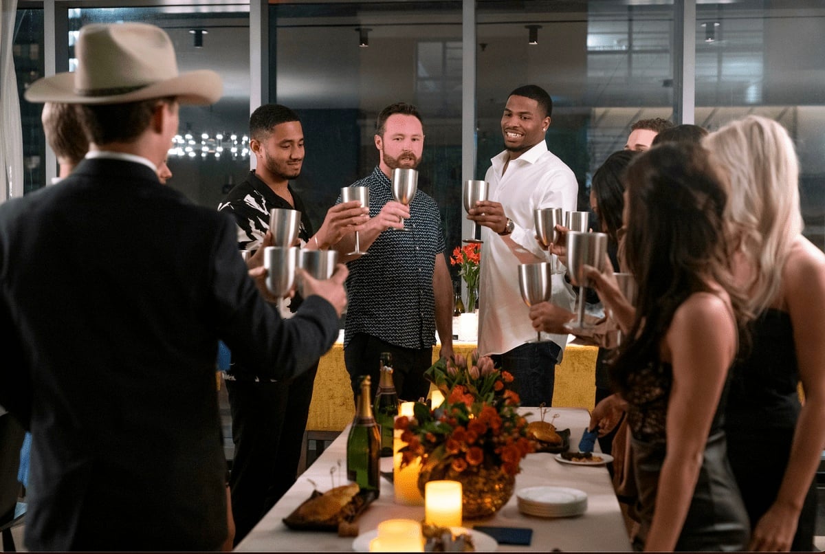 The Ultimatum cast stand around a table with metal cups and prepare to cheers.