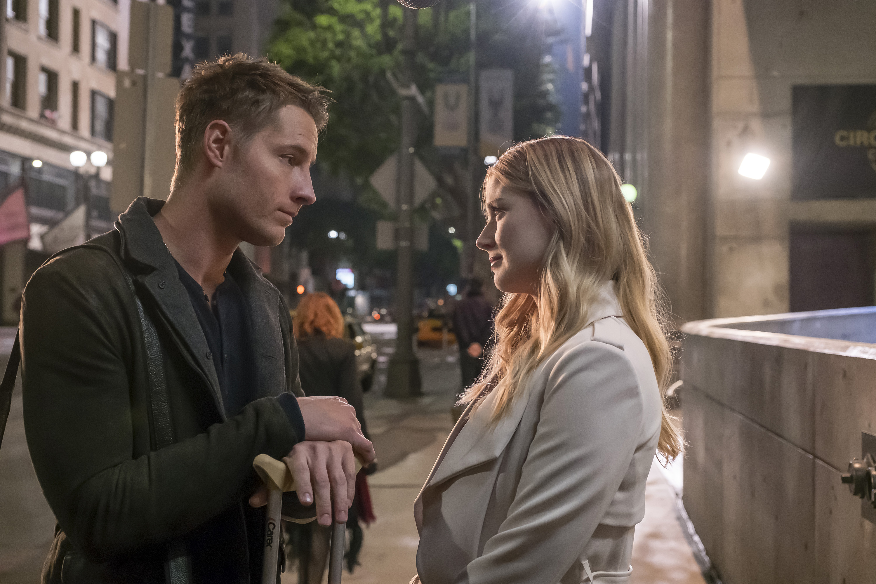 'This Is Us' Season 6 Episode 13 stars Justin Hartley and Alexandra Breckenridge, in character as Kevin and Sophie, share a scene. Kevin wears a dark gray coat over a blue shirt. Sophie wears a white coat.