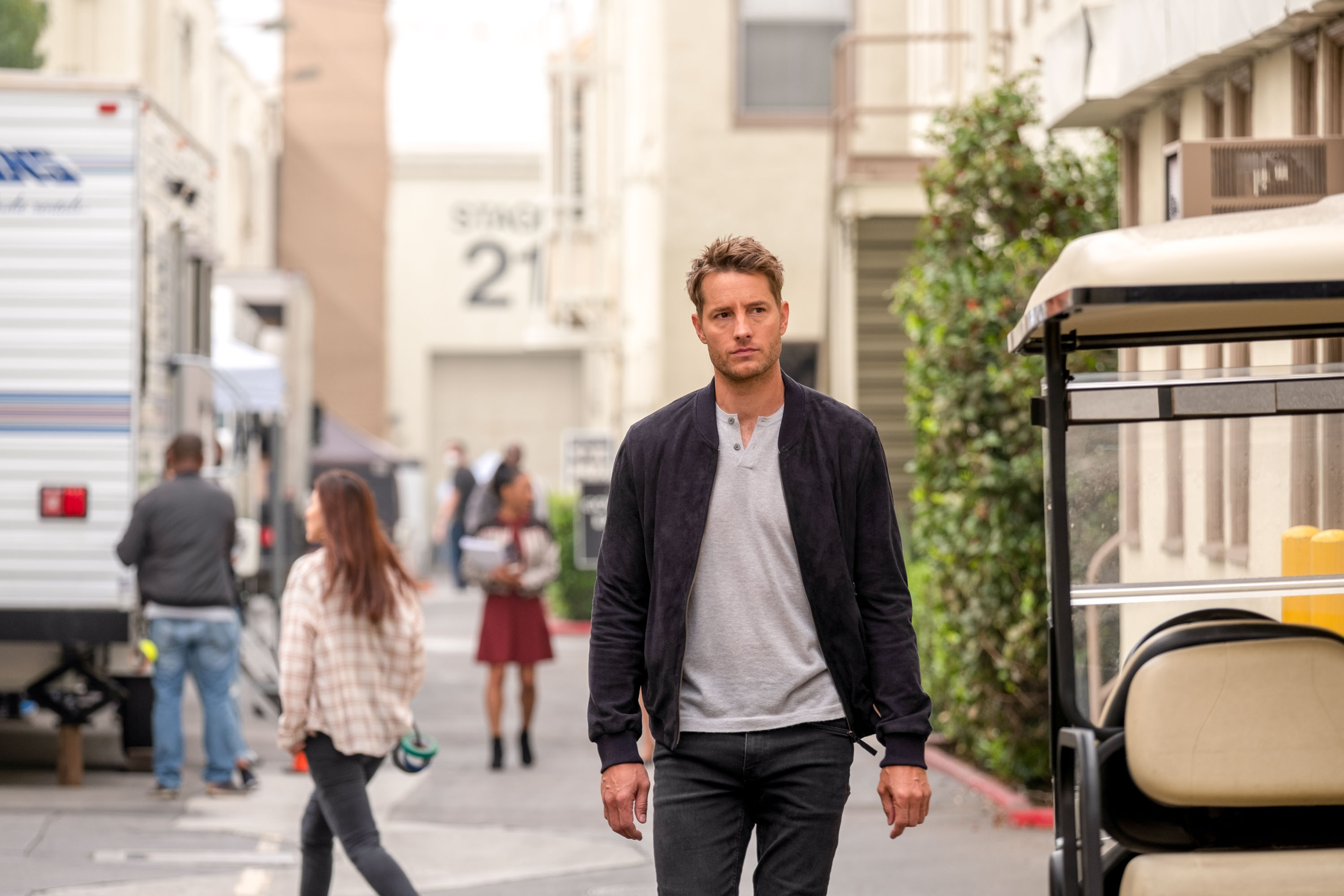 'This Is Us' star Justin Hartley, in character as Kevin Pearson, wears a black jacket over a light gray shirt and black pants while walking through a production studio.