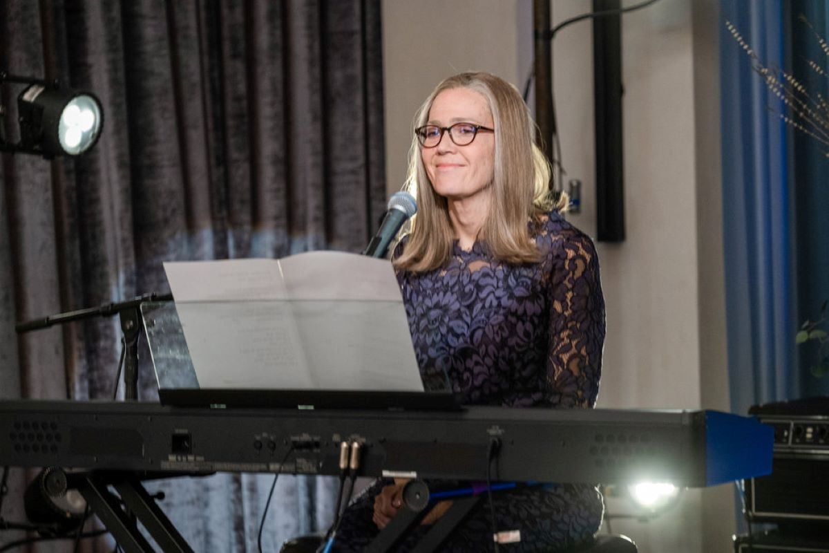 Mandy Moore, in character as Rebecca in 'This Is Us' Season 6 Episode 14, sings a song and plays the keyboard. Rebecca wears a dark blue floral dress. She will appear in the 'This Is Us' Season 6 finale.