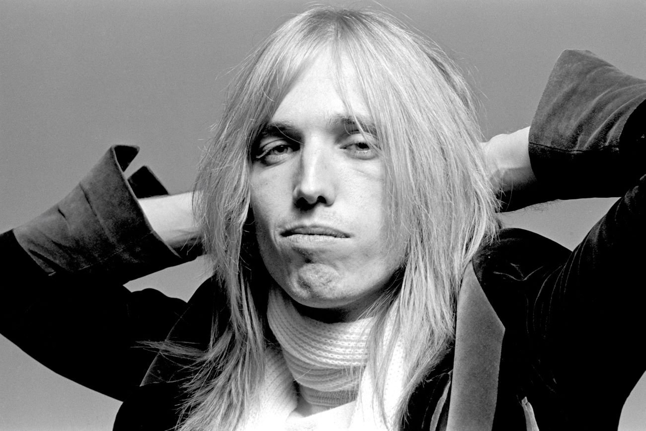 A black and white picture of Tom Petty wearing a scarf and clasping his hands behind his head.