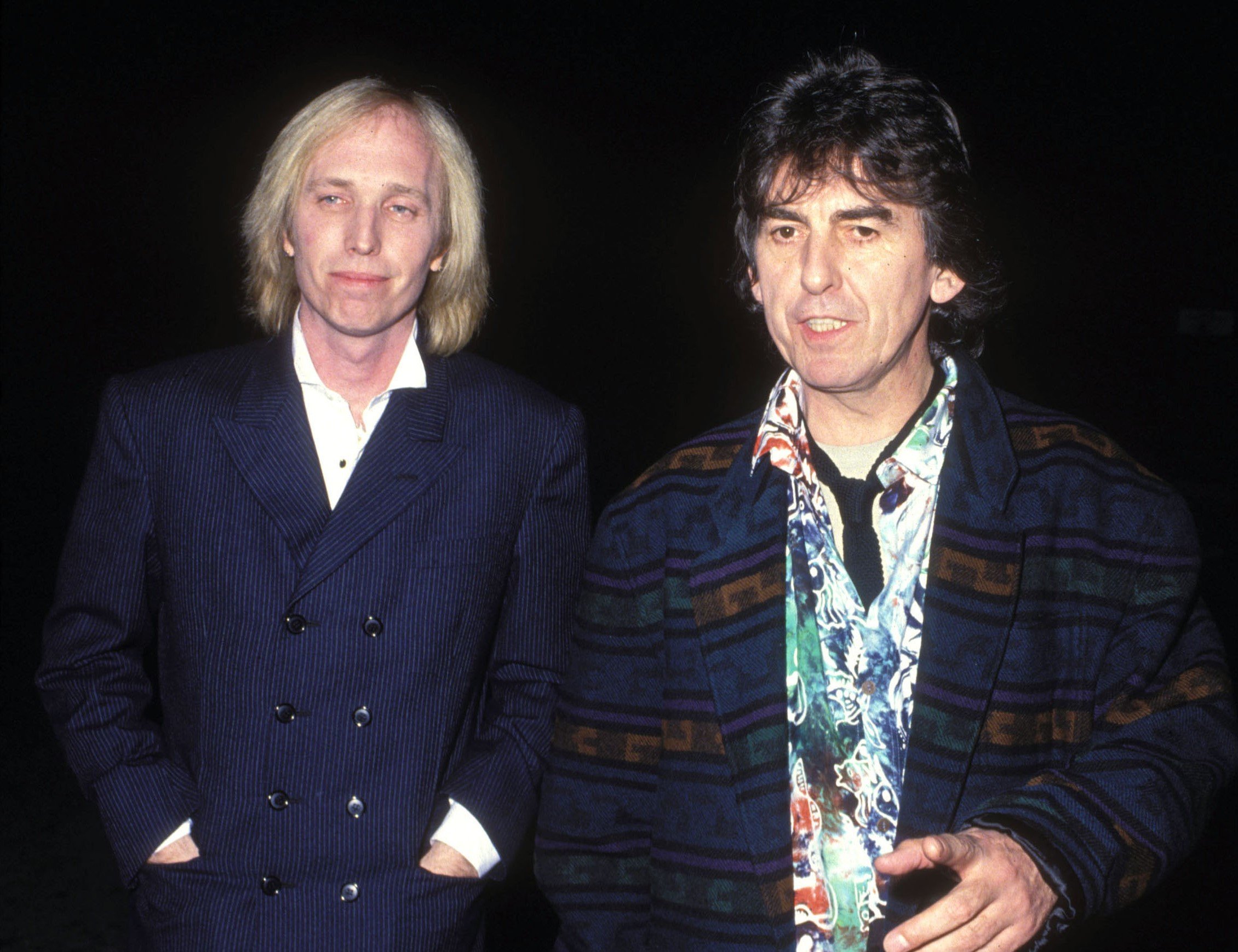 Tom Petty and George Harrison wear jackets and walk outdoors at night.