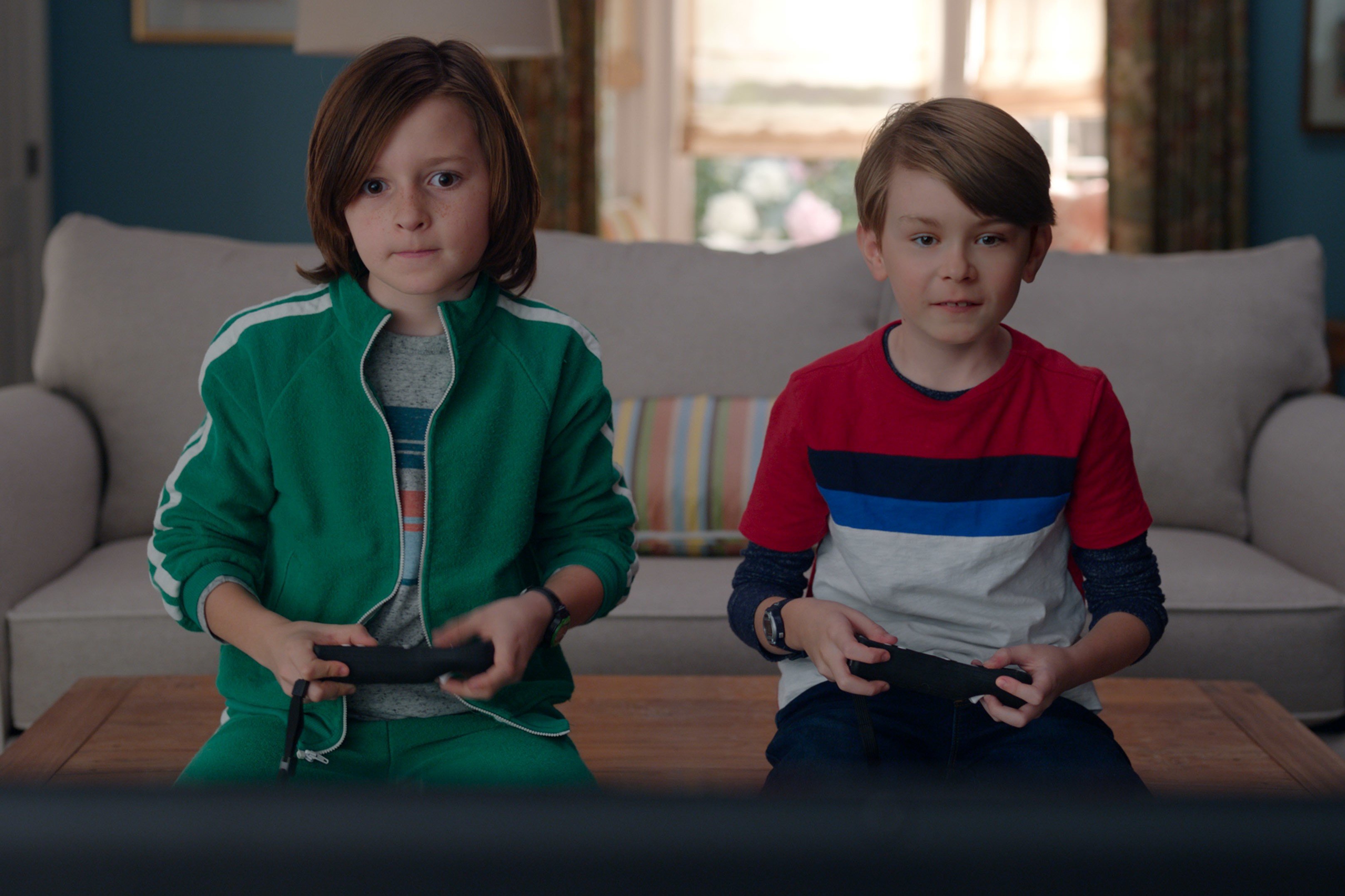 'WandaVision' stars Jett Klyne and Julian Hilliard, who will reprise their roles as Tommy and Billy in 'Doctor Strange 2,' share a scene where they play video games. Tommy wears a green and white tracksuit. Billy wears a red, blue, and gray shirt and jeans.