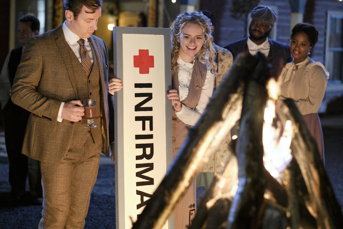 Mike standing next to Faith as she hold the infirmary sign in front of the bonfire in 'When Calls the Heart' Season 9 Episode 7