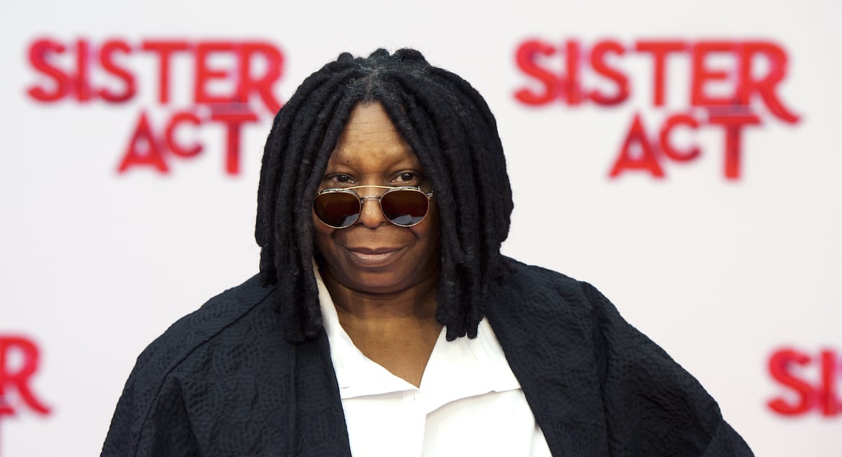 Whoopi Goldberg wears sunglasses as she poses in front of the ‘Sister Act’ logo