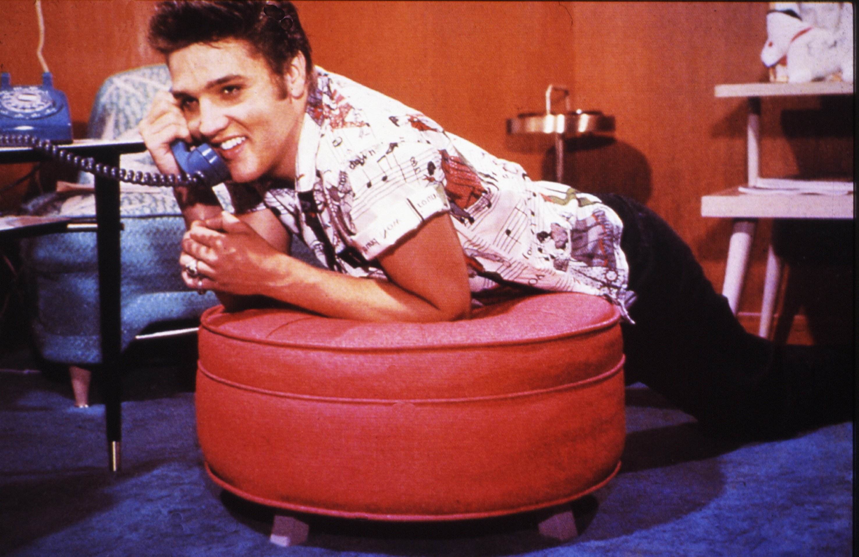 "Blue Suede Shoes" singer Elvis Presley holding a telephone while leaning on a futon