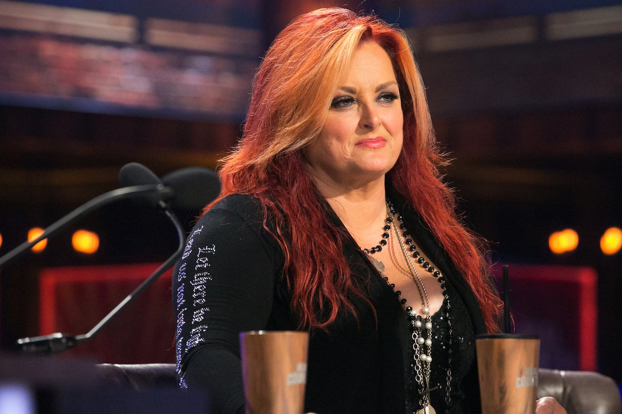 Wynonna Judd in a black jacket, seated at a table in front of a microphone