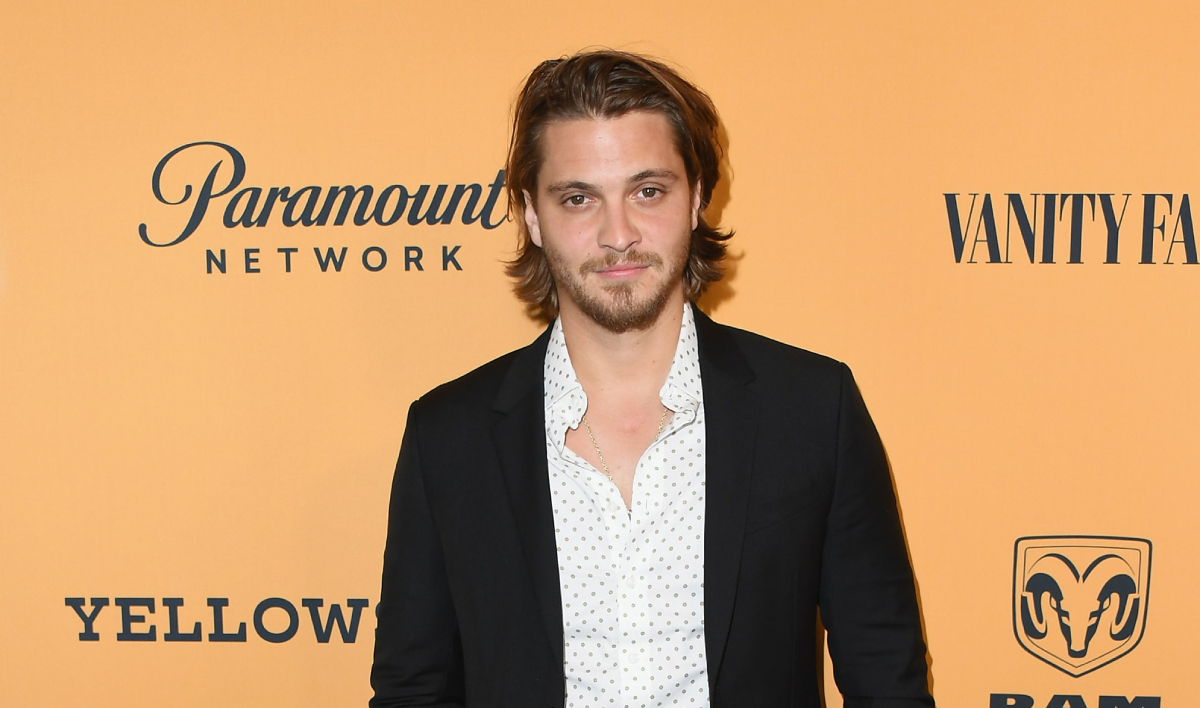 Luke Grimes wearing a white shirt and black suit poses as he attends the premiere of Paramount Pictures' "Yellowstone" at Paramount Studios on June 11, 2018 in Hollywood, California