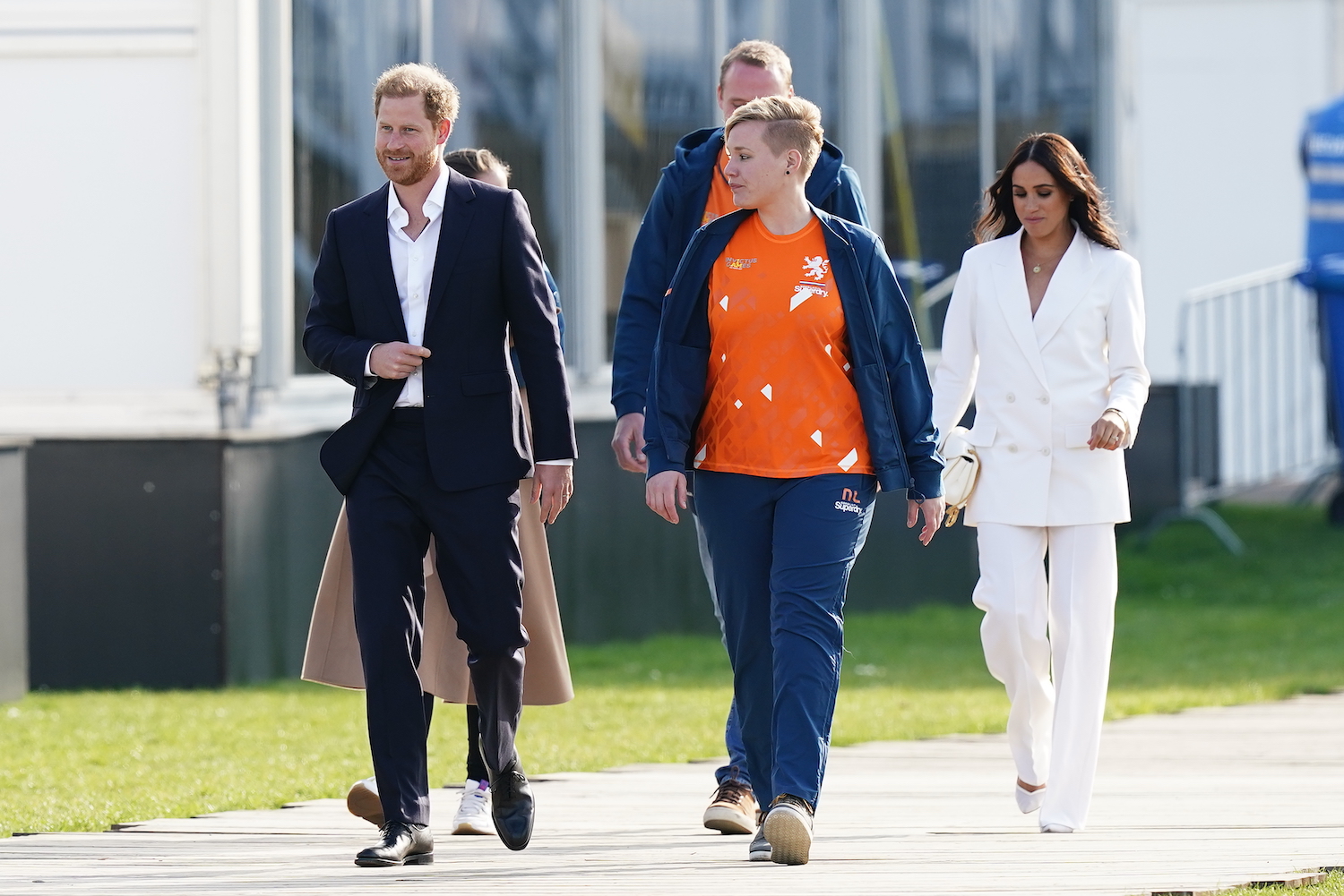 Prince Harry wears a dark suit and Meghan Markle wears a white pantsuit while walking at a reception for the Invictus Games