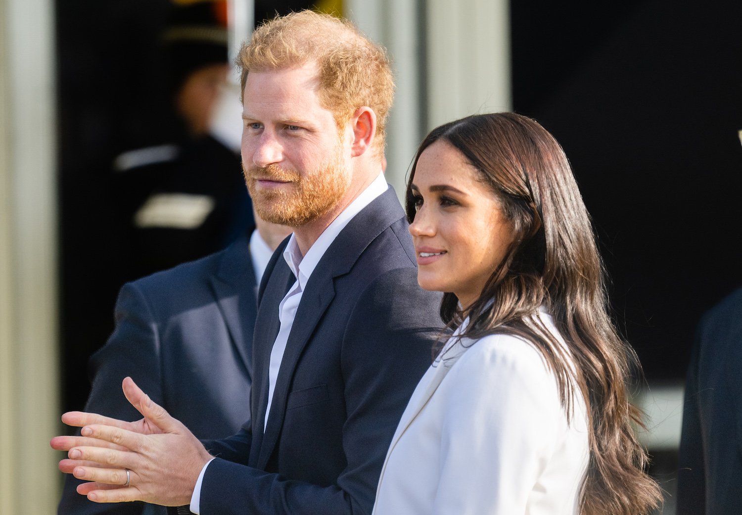Prince Harry wears a dark jacket and Meghan Markle wears a white pant suit during their appearance at the Invictus Games