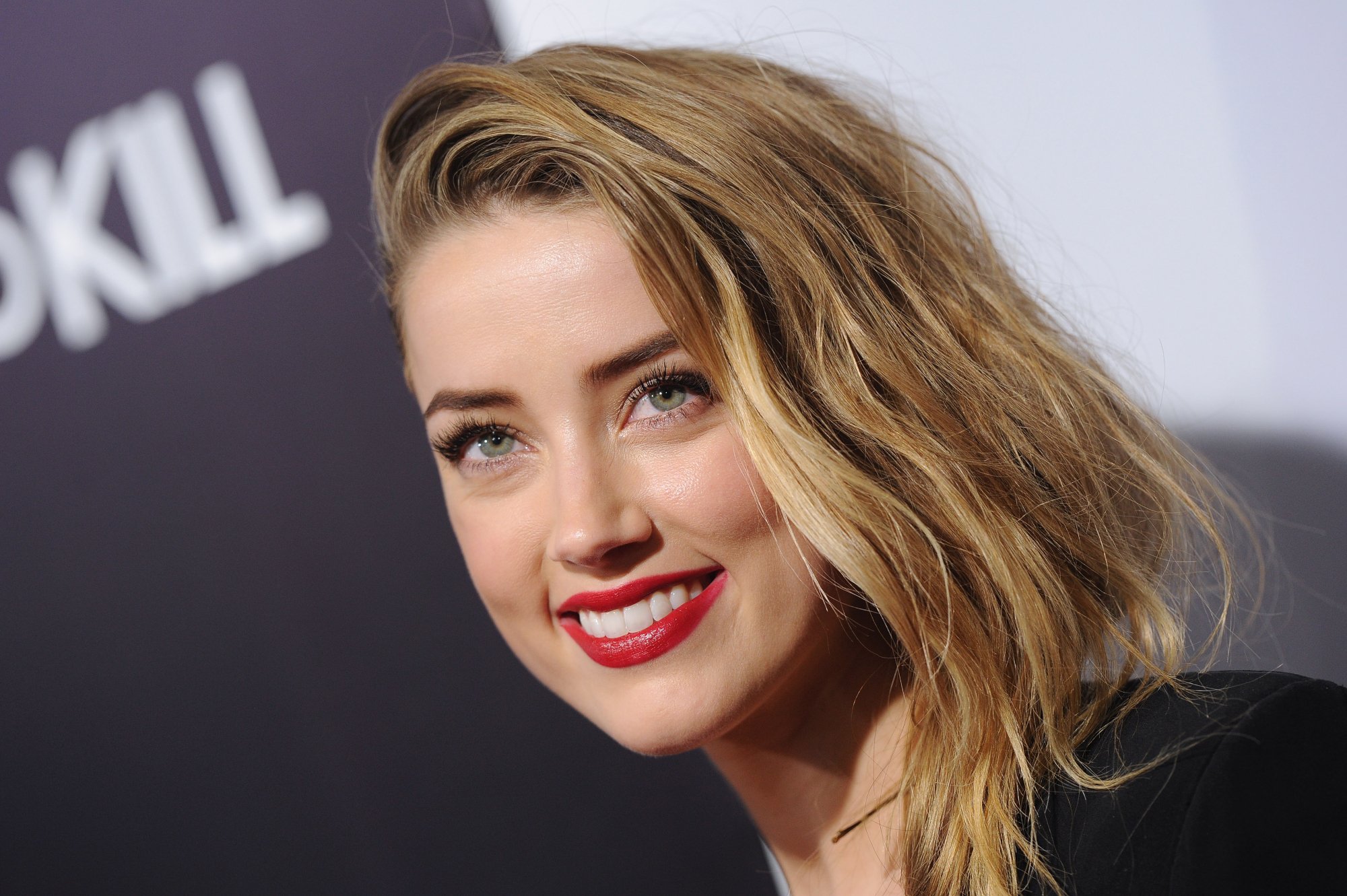 '3 Days to Kill' actor Amber Heard, who starred alongside Kevin Costner. She smiles with red lipstick on in front of a step and repeat.