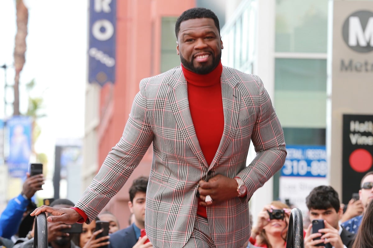50 Cent posing while wearing a red suit and turtle neck.