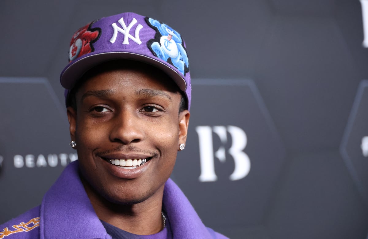A$AP Rocky wears a purple jacket and Yankees hat while smiling at a Fenty Beauty event.