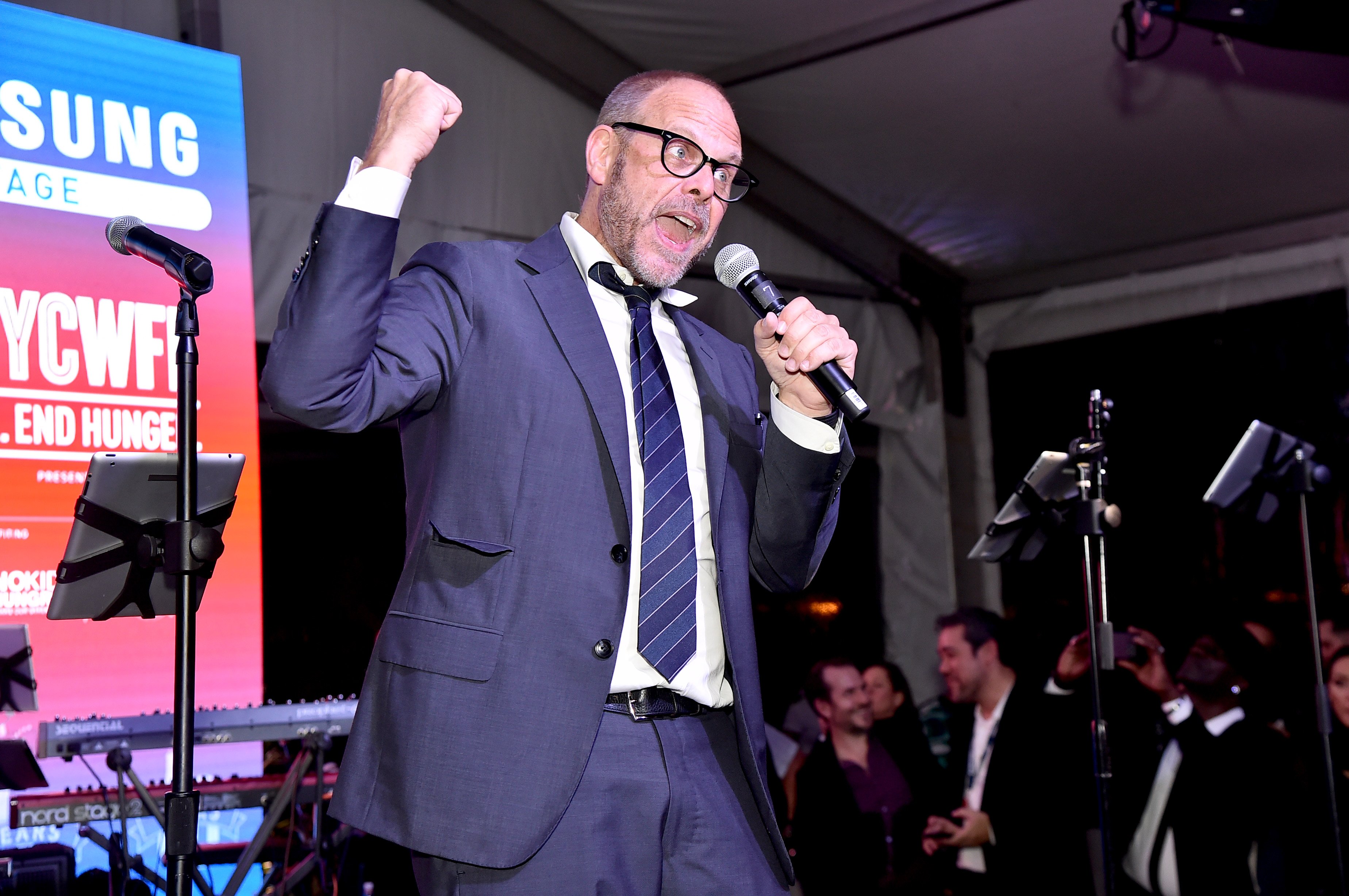 Culinary personality Alton Brown wears a suit and tie onstage at a Food Network event in this photograph.