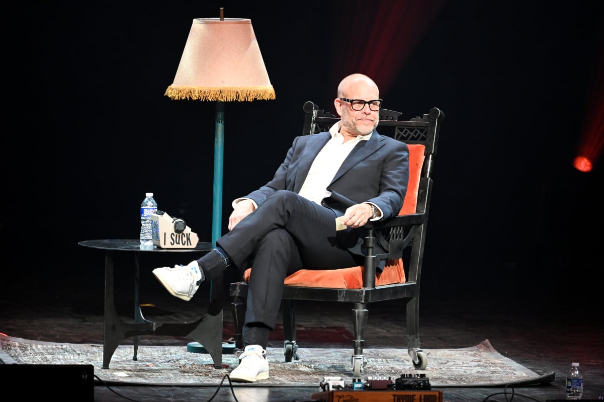 Former Food Network star Alton Brown sitting in a chair next to a lamp