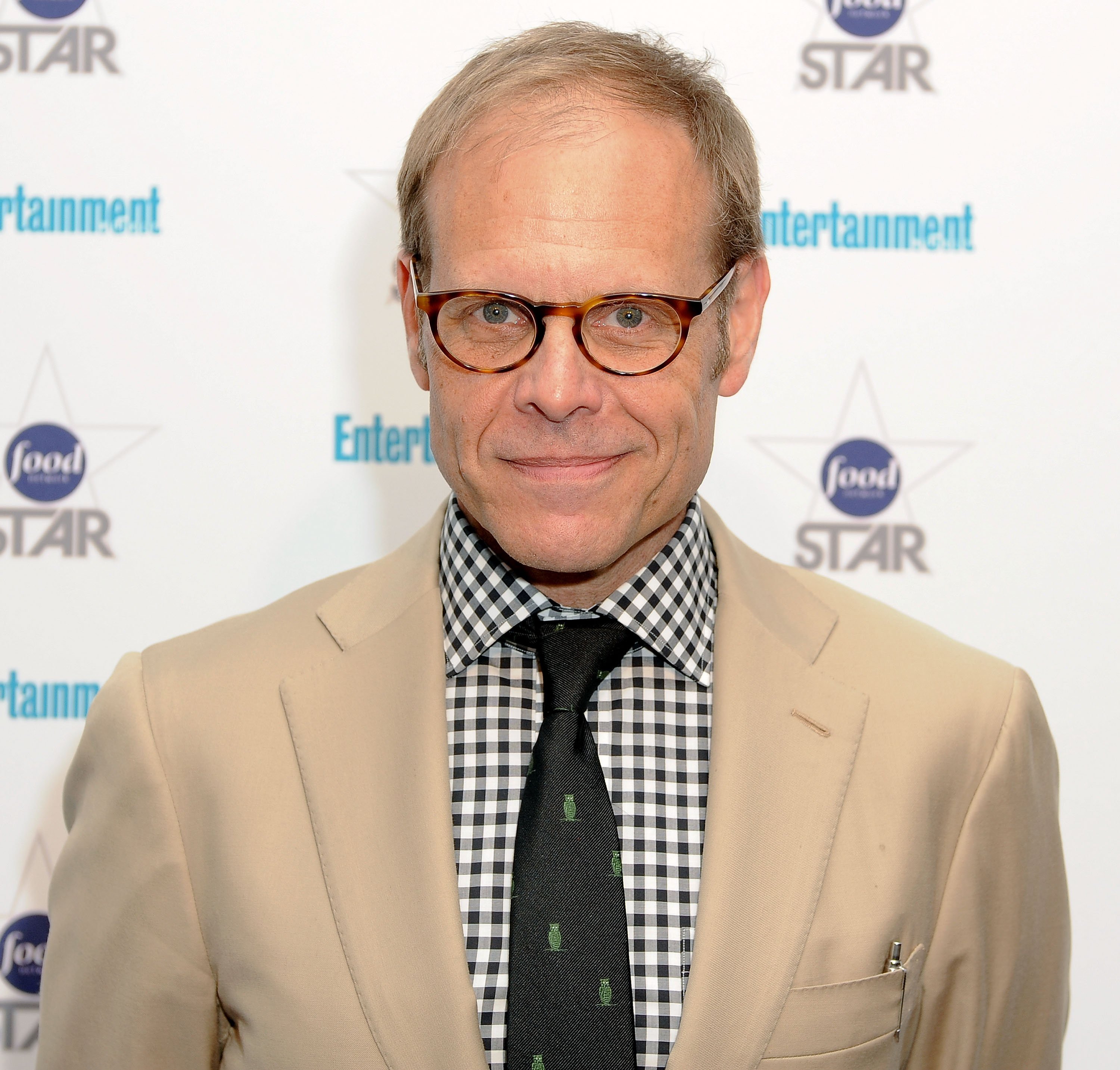 Alton Brown poses for a photo in a light-colored jacket.