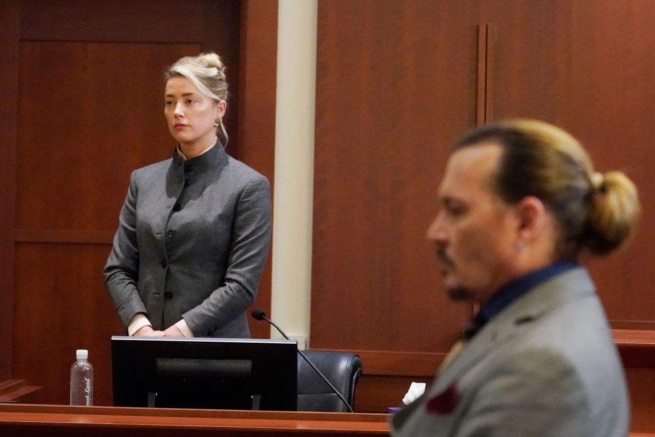 Amber Heard stands in the courtroom while Johnny Depp sits nearer to the camera.