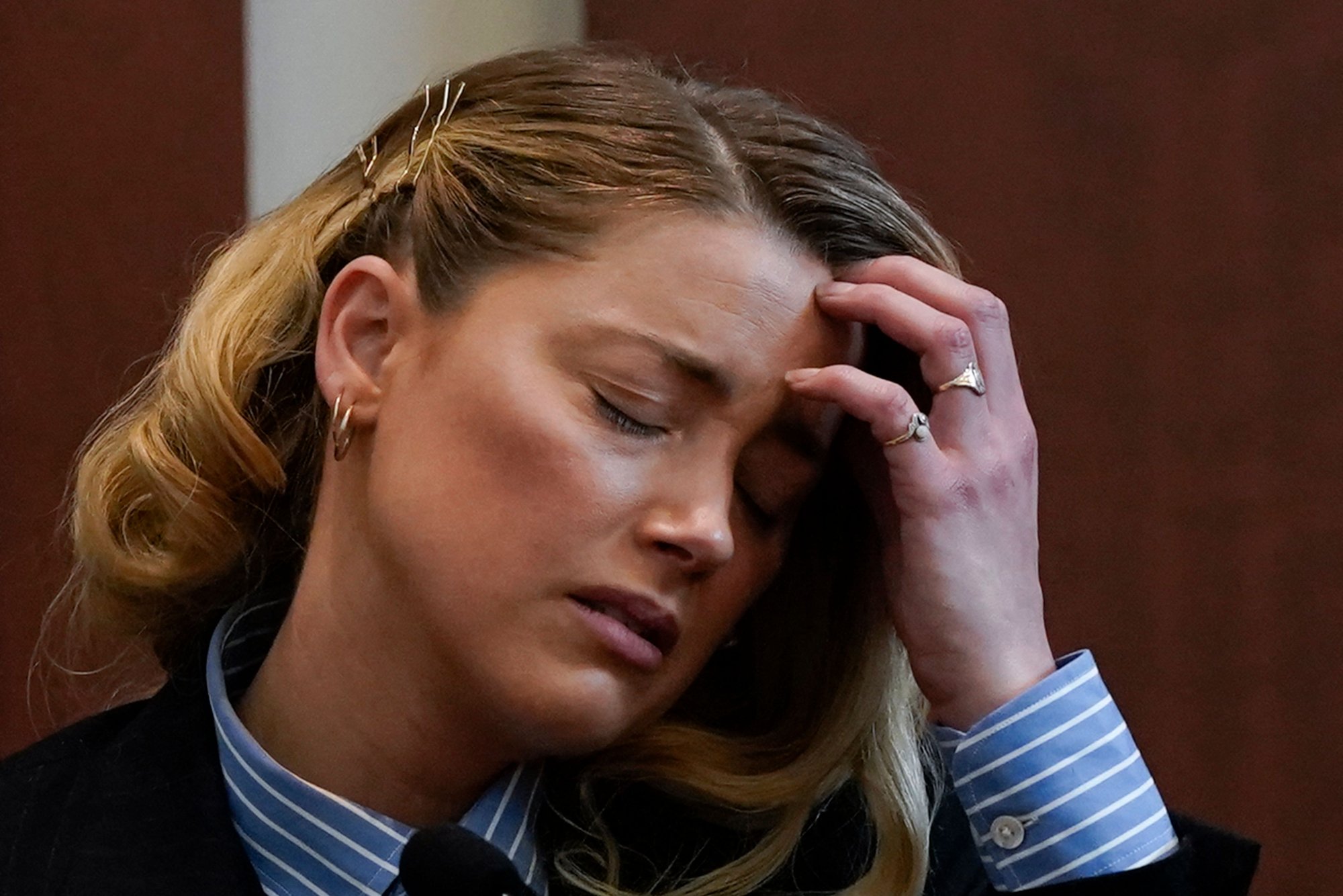 Amber Heard in trial resulting in memes. She looks distressed, wearing a suit, with her hand on her forehead and her eyes closed.