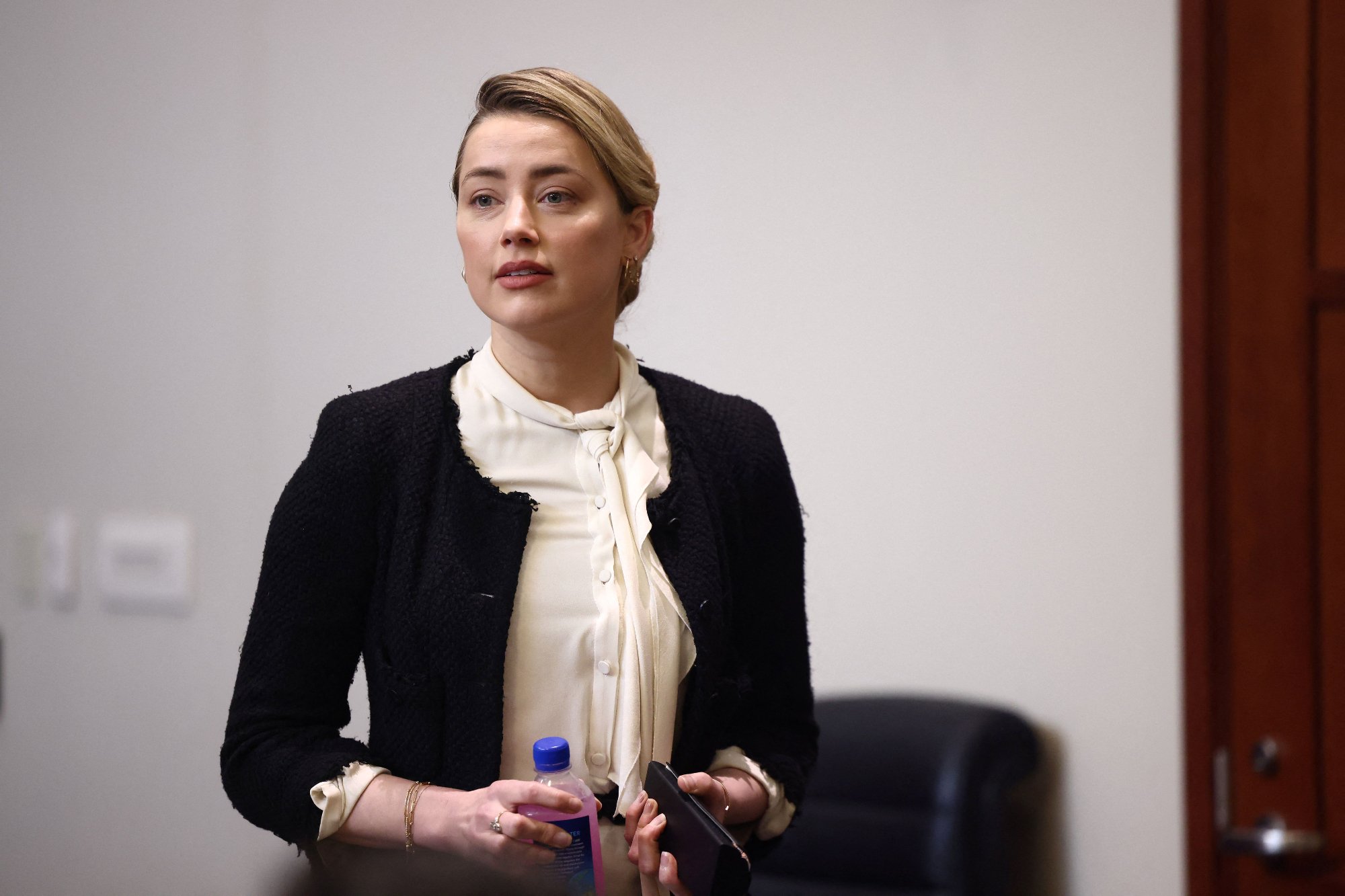 Amber Heard standing holding a beverage and wearing white and black