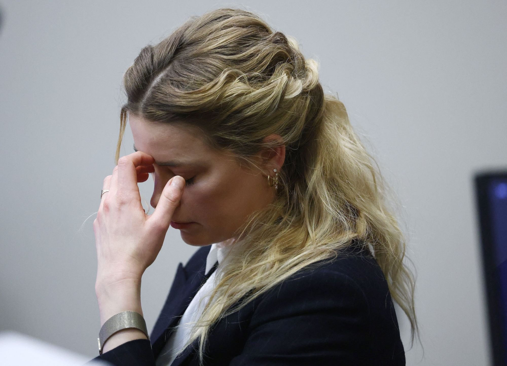 Amber Heard with a hand up to her face while she listens to an audio clip of an argument between her and Johnny Depp