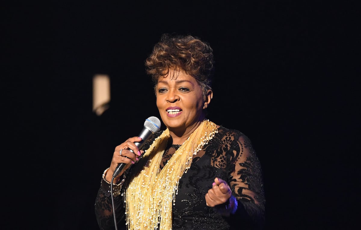 Anita Baker, who got her masters thanks to Chance the Rapper, wearing a gold scarf and holding a microphone