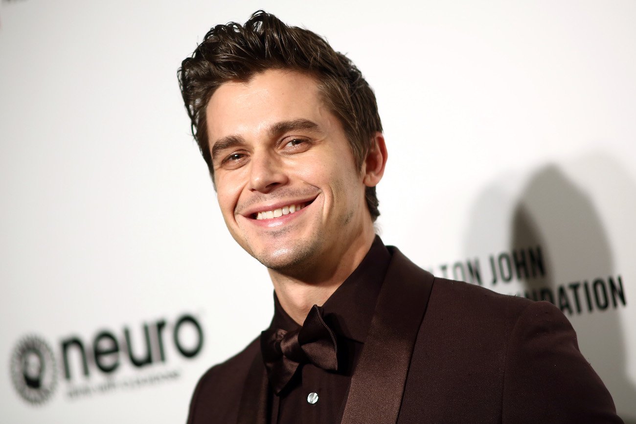 Antoni Porowski wearing a gray outfit and smiling in front of a white background