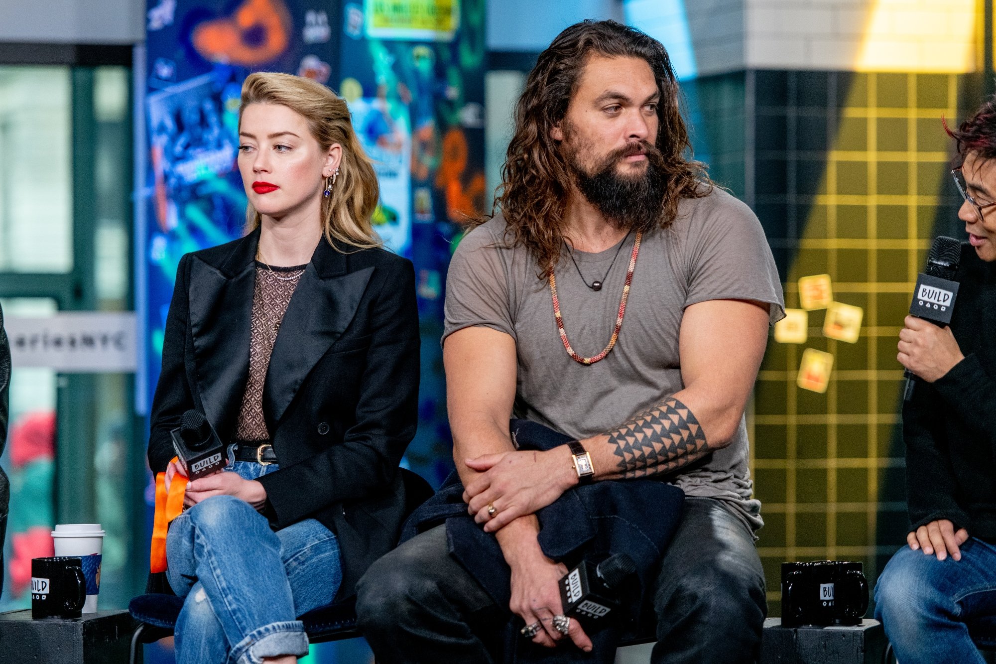 'Aquaman' Amber Heard and Jason Momoa sit holding microphones looking in opposite directions sitting next to each other