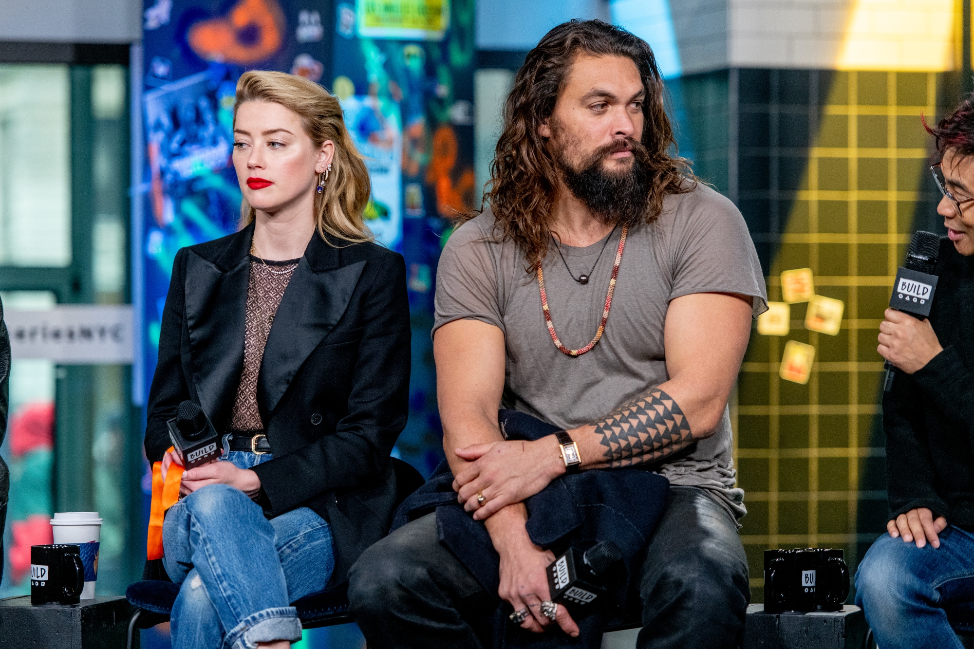 'Aquaman' Amber Heard and Jason Momoa sit holding microphones looking in opposite directions sitting next to each other