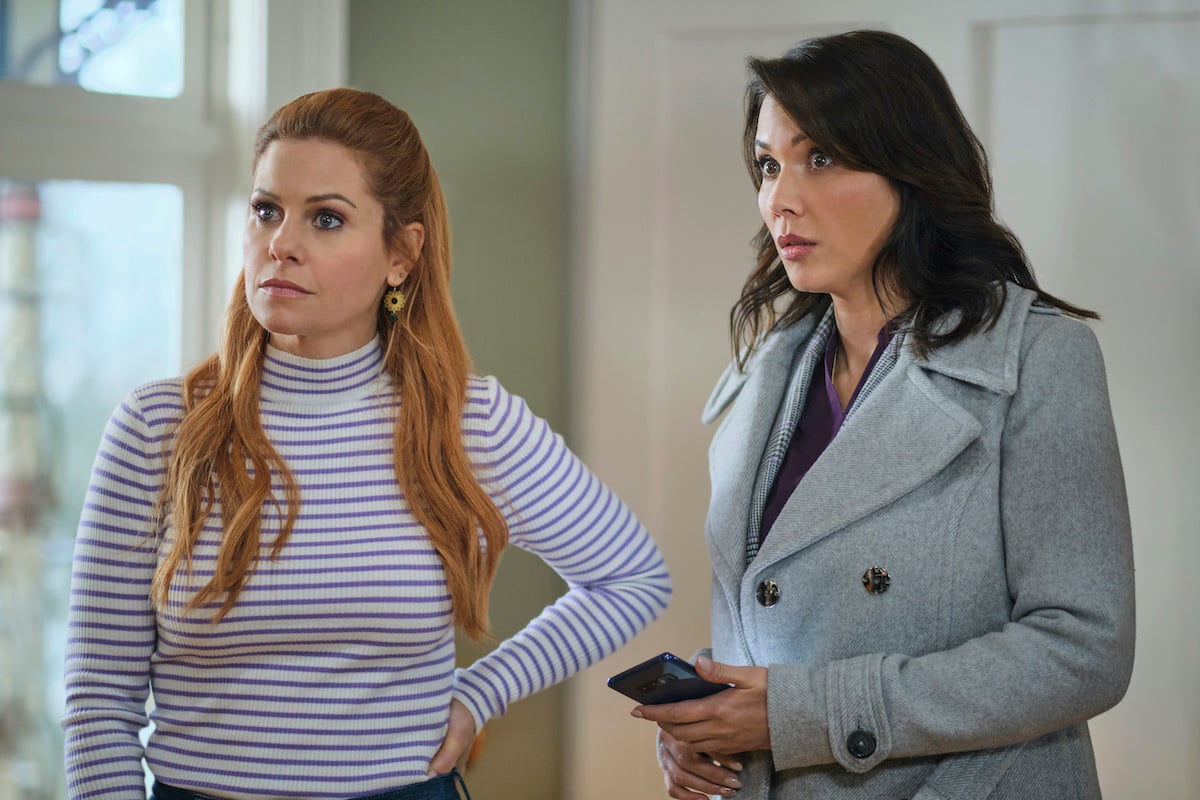 Candace Cameron Bure, with her hand on her hip, standing next to Lexa Doig in 'Aurora Teagarden Mysteries: Haunted by Murder'