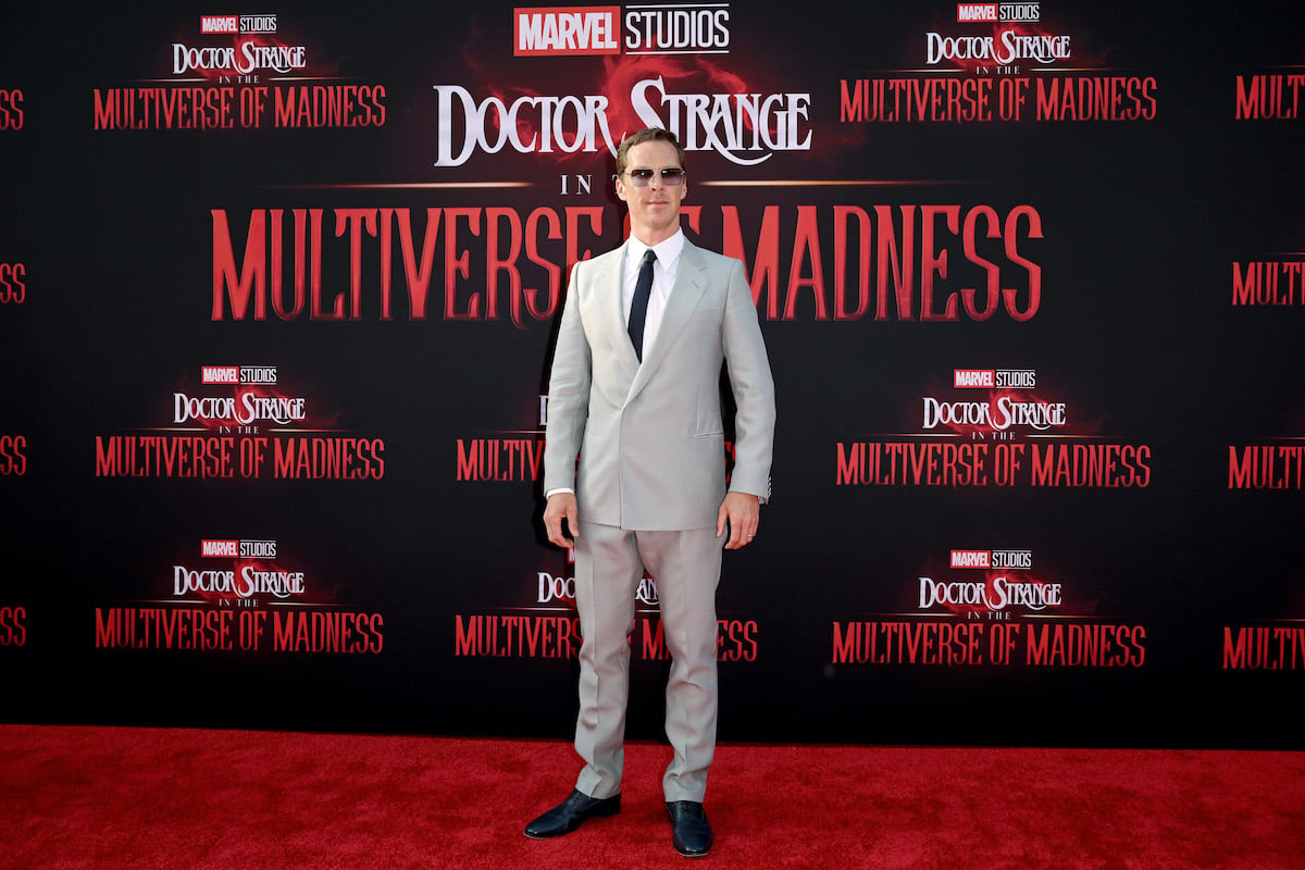‘Doctor Strange in the Multiverse of Madness’ star Benedict Cumberbatch wears a suit and poses in front of the film’s logo
