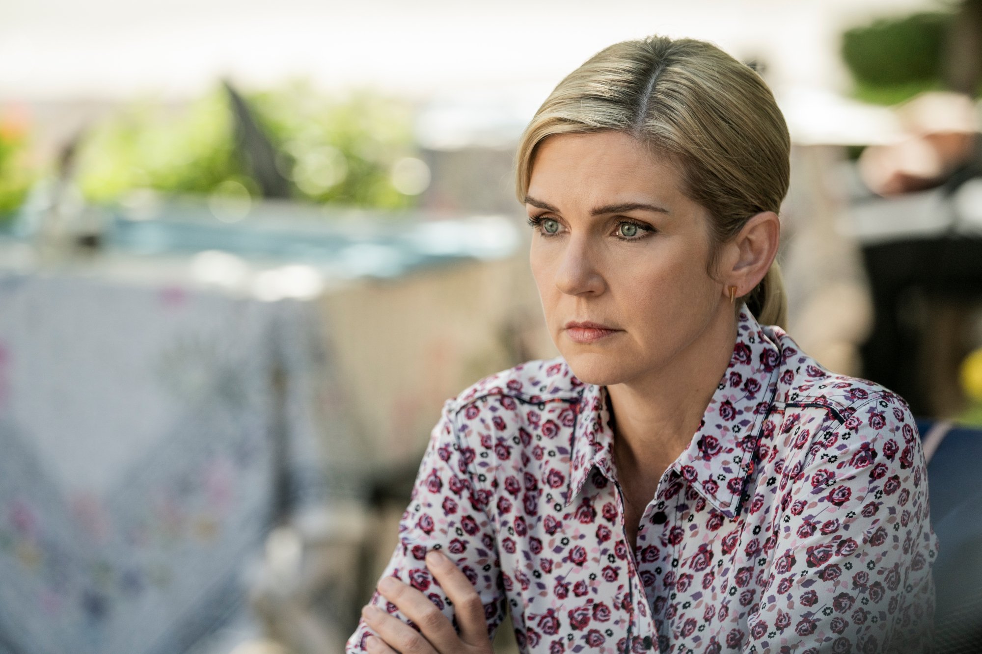 Rhea Seehorn as Kim Wexler in 'Better Call Saul' Season 6 Episode 4. She's sitting at a table, her hair is in a ponytail, and she's wearing a white and red blouse.