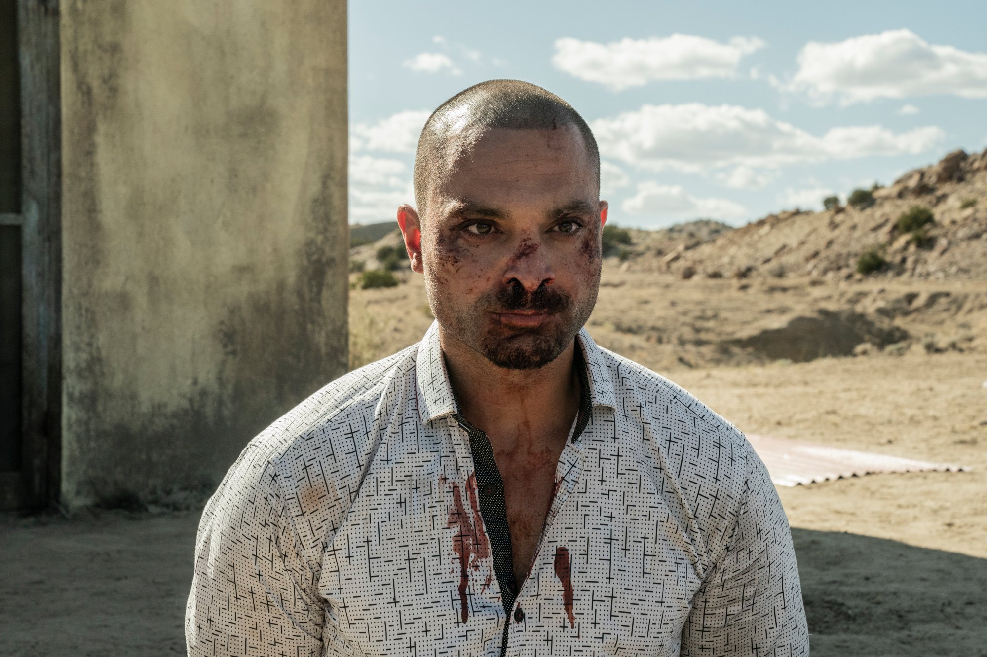 Michael Mando as Nacho Varga in 'Better Call Saul' Season 6 Episode 3. His face and clothes are bloody, and he's kneeling in the desert.