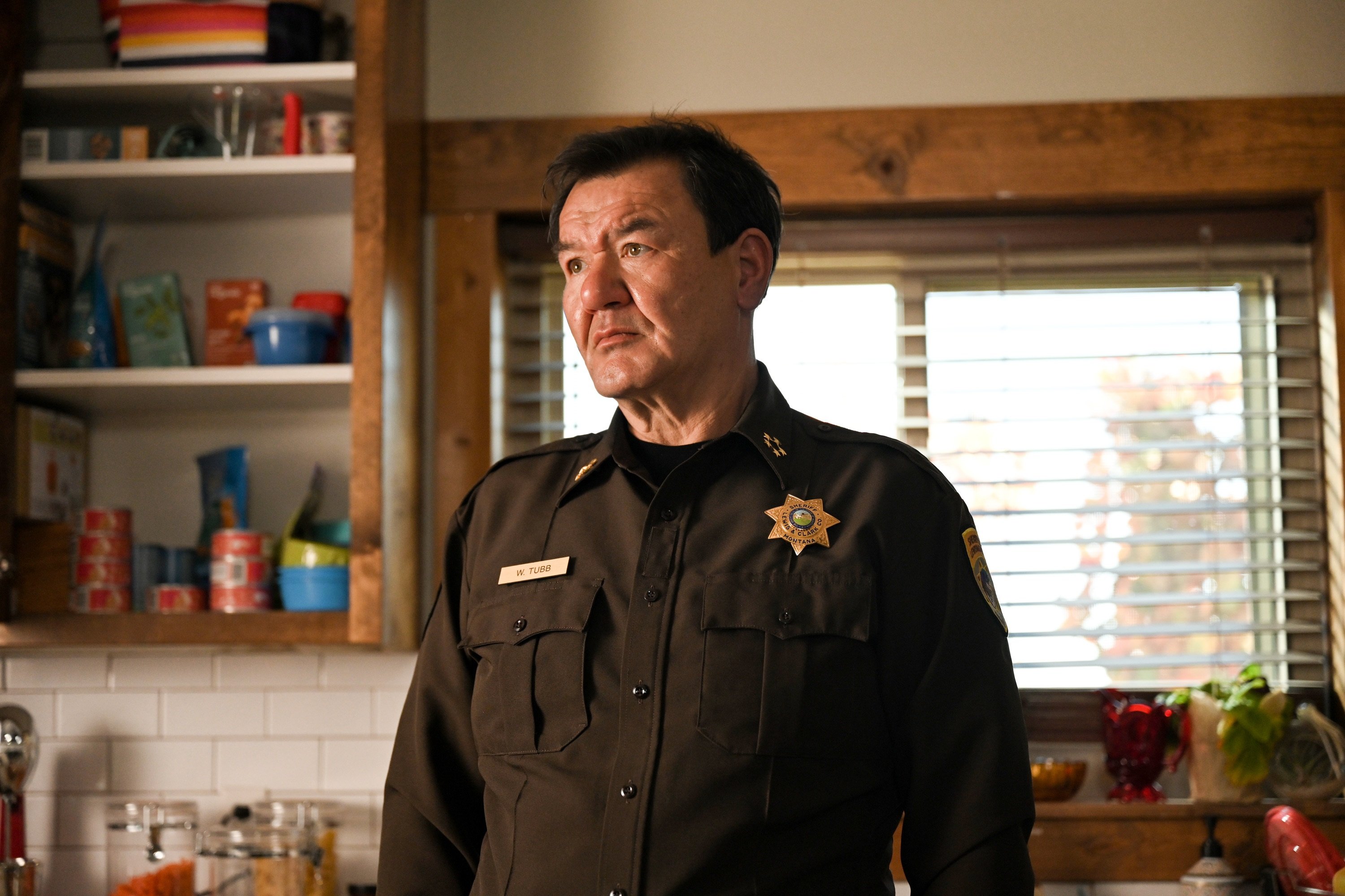 'Big Sky' Patrick Gallagher stares at something while standing in a kitchen as Sheriff Tubb