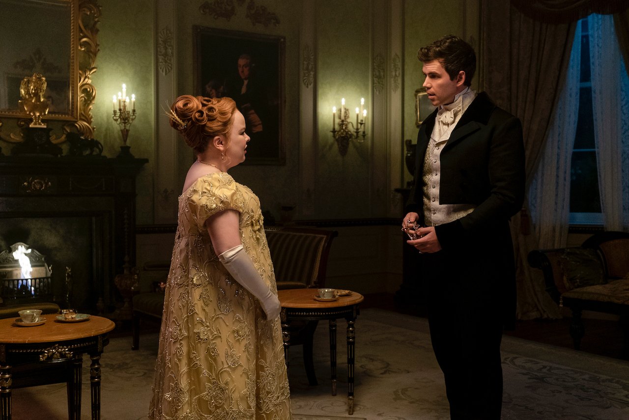 (L to R) Nicola Coughlan as Penelope Featherington and Luke Newton as Colin Bridgerton in 'Bridgerton' talk to each other privately.