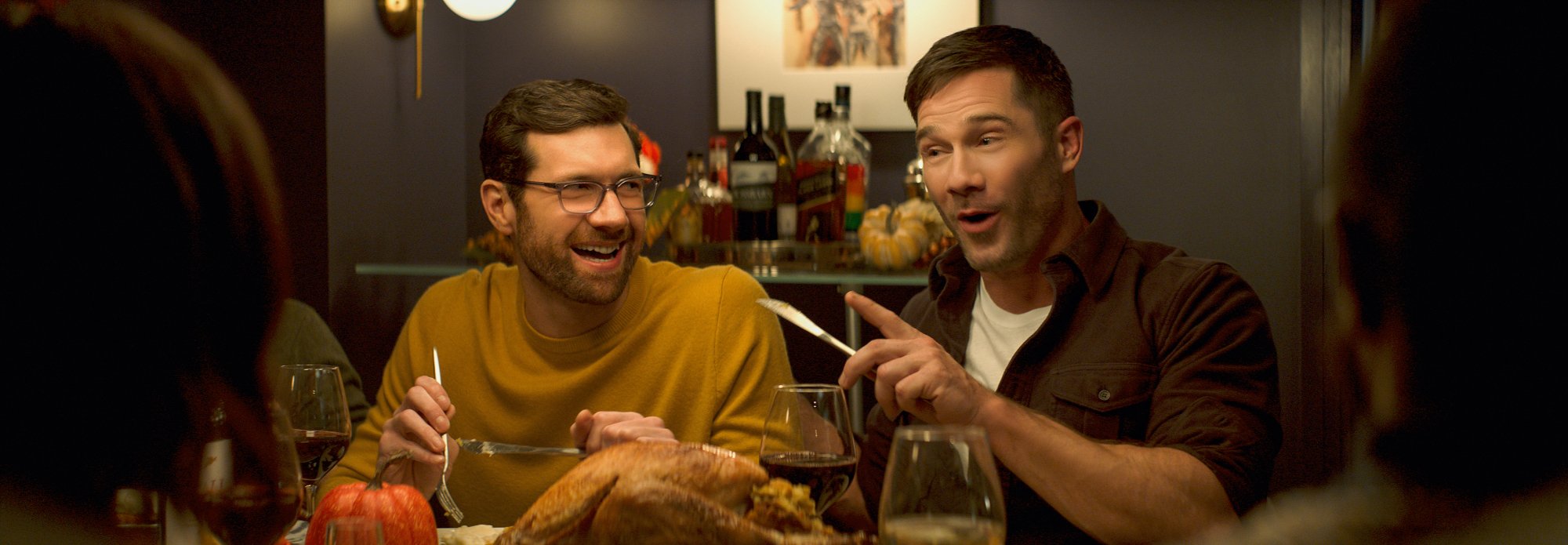 'Bros' Billy Eichner as Bobby and Luke Macfarlane as Aaron smiling, holding dinner utensils with food in front of them