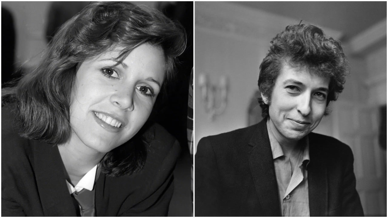 A black and white photo of Carrie Fisher smiling and wearing a collared shirt. Bob Dylan smiles and wears a blazer.