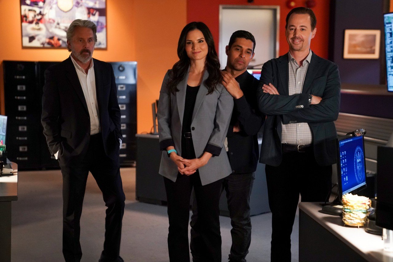 The NCIS cast stands in the office together.