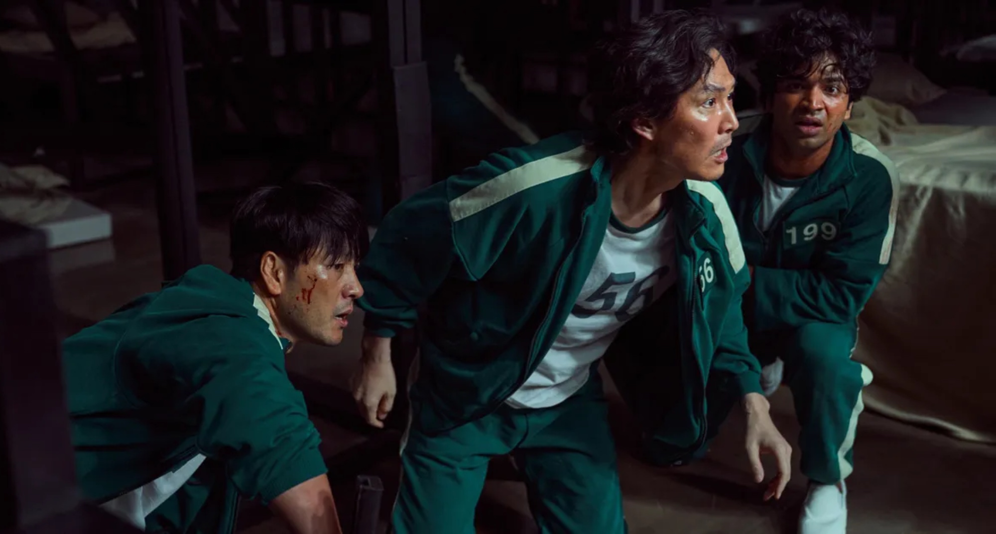Characters Sang-woo, Gi-hun, and Ali wearing green track suits and looking concerned in 'Squid Game,' which originally was to be a webtoon.