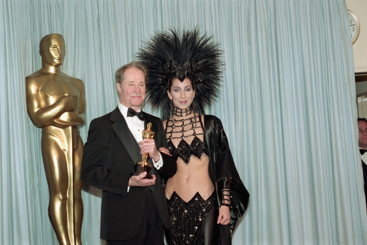 Don Ameche holds the Best Supporting Actor Oscar award for his role in Cocoon, with award presenter Cher, who is wearing an unusual Bob Mackie evening gown with a feather headdress