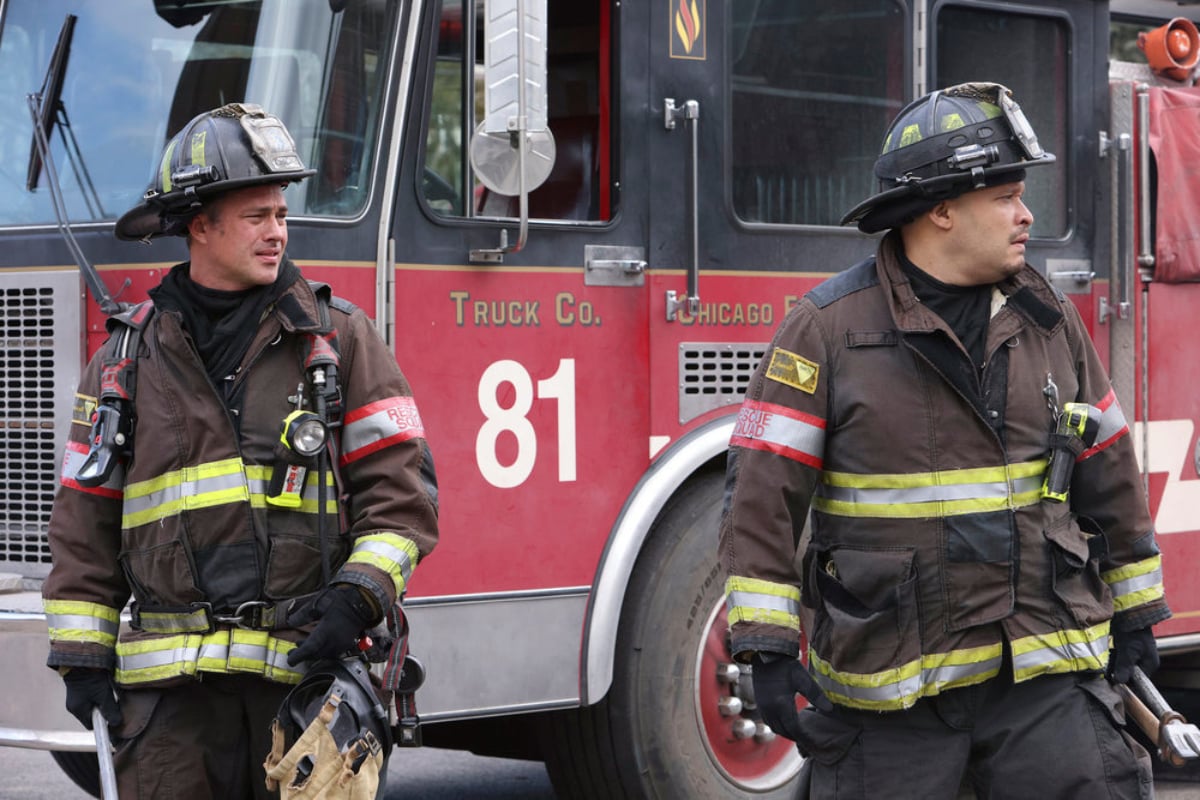 Taylor Kinney as Kelly Severide and Joe Minoso as Joe Cruz in Chicago Fire Season 1. The men stand outside a fire truck. 
