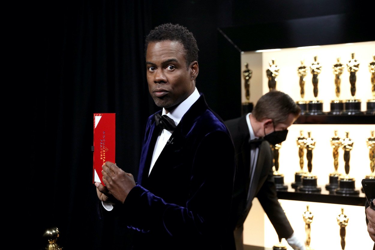 Chris Rock stands backstage next to Oscar statuettes at the 2022 Academy Awards. Rock hosting the 2023 Oscars is a rumor that reeks of desperation.