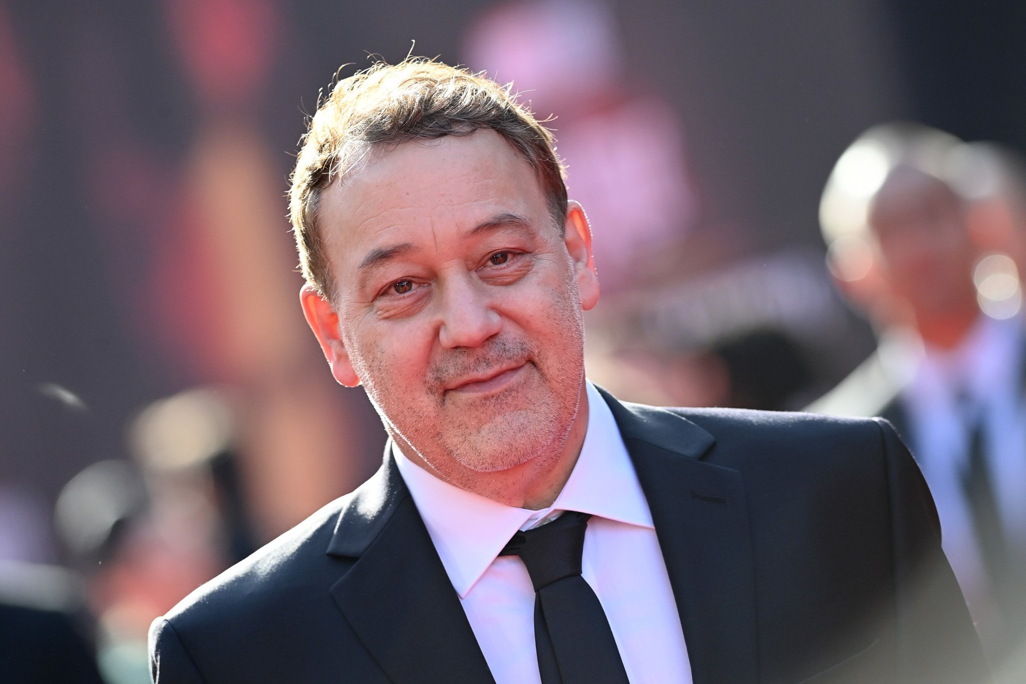 Director Sam Raimi at the premiere for 'Doctor Strange 2.' He's wearing a white shirt, black suit, and black tie and smiling at the camera.