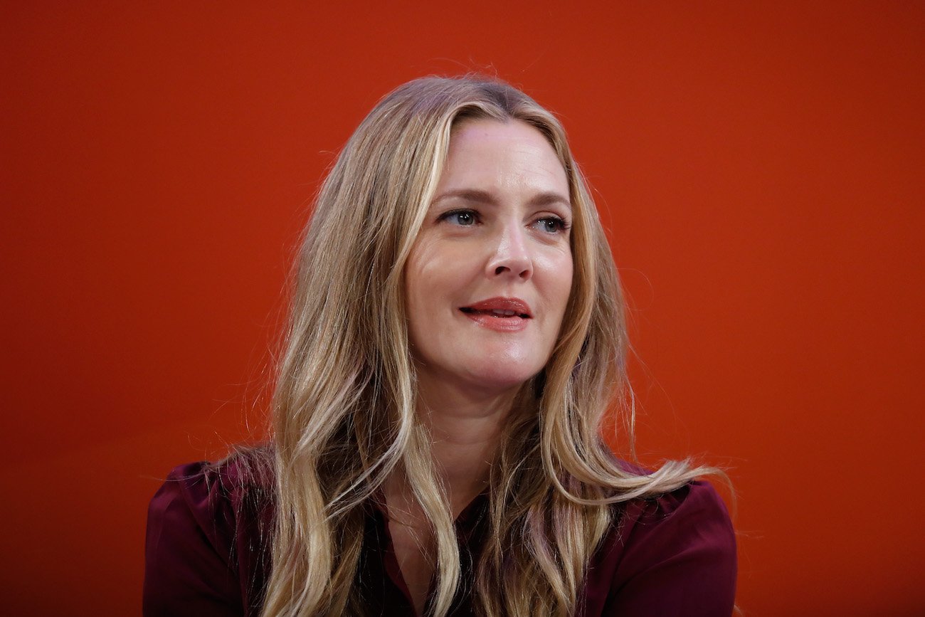 Drew Barrymore in front of a red background and looking toward the right side of the photo