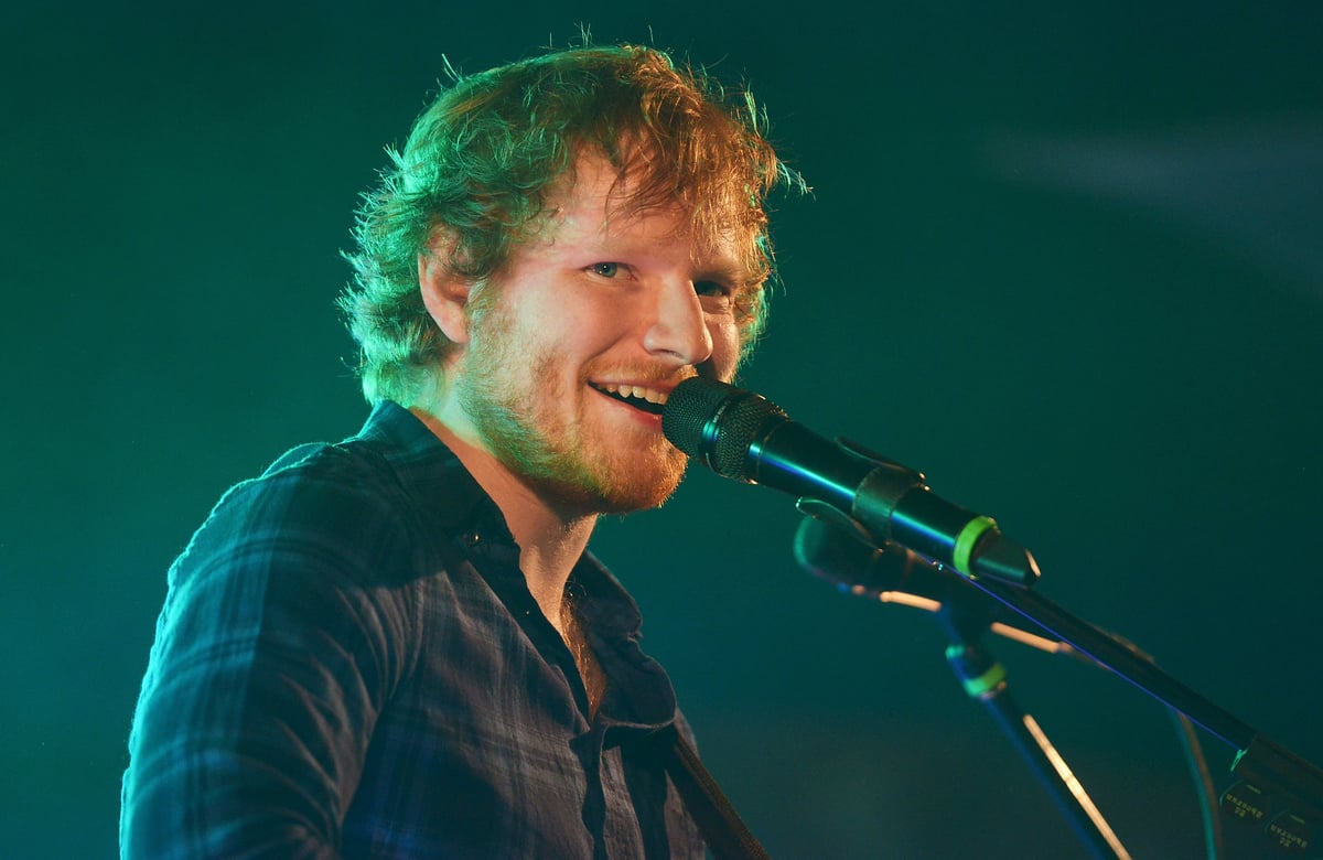 Ed Sheeran smiles while singing into a microphone on stage.