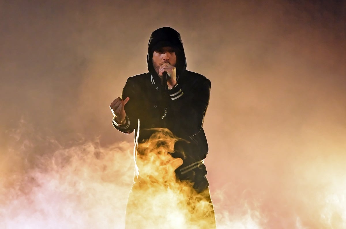 Eminem rapping while wearing a black jacket and black clothes.