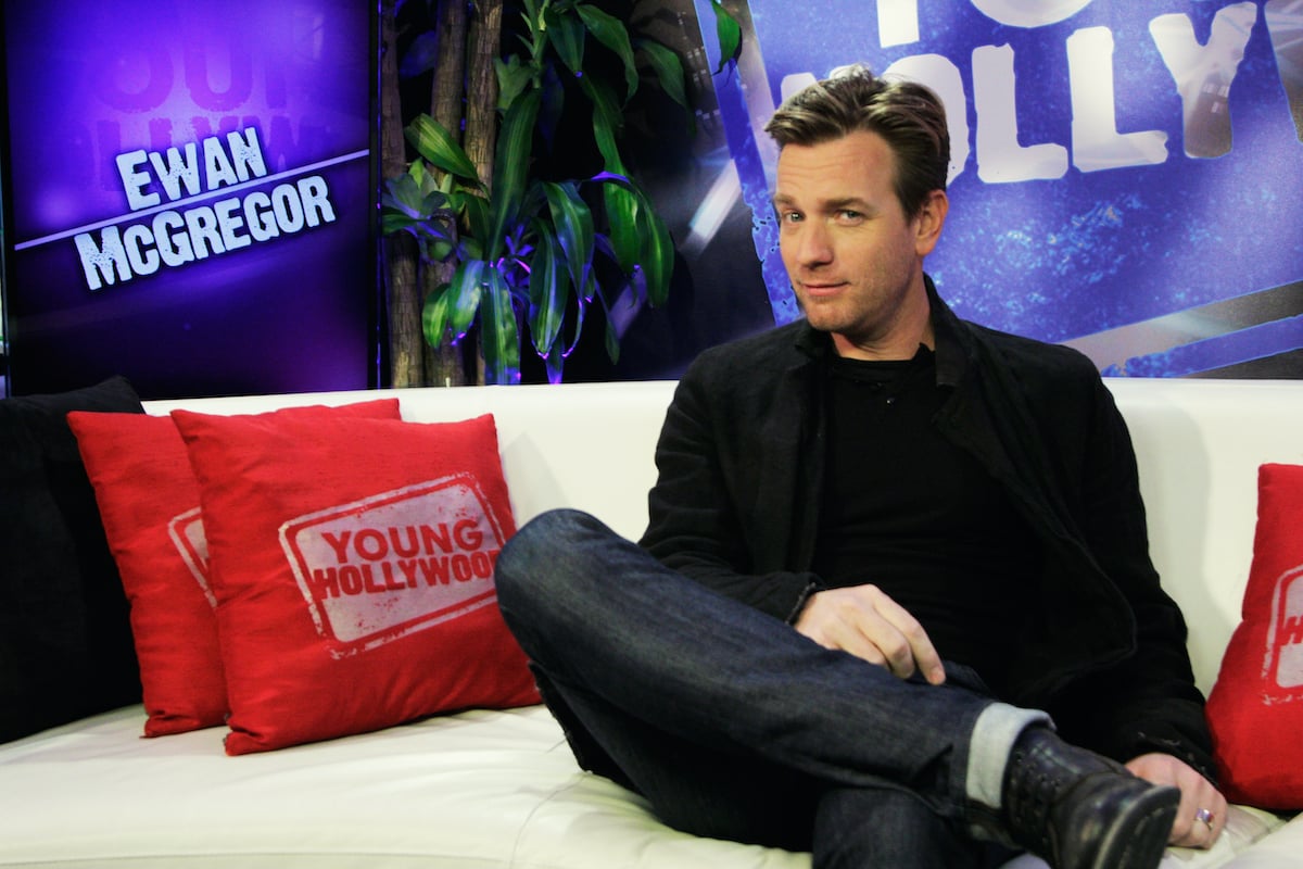 Ewan McGregor smiles and looks at the camera while sitting on a white couch