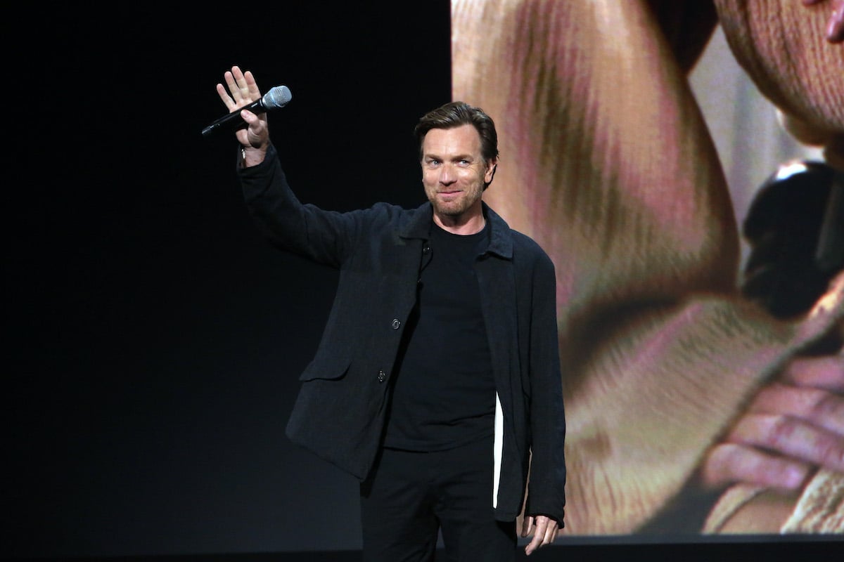 Ewan McGregor dressed in black smiles on stage and waves