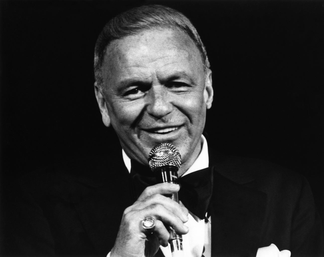 A black and white picture of Frank Sinatra wearing a tuxedo and holding a microphone.